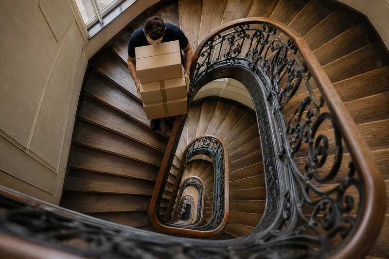 Déménageur montant des cartons dans une cage d'escalier ancienne